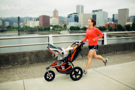 Mother running with baby in stroller on city bridge